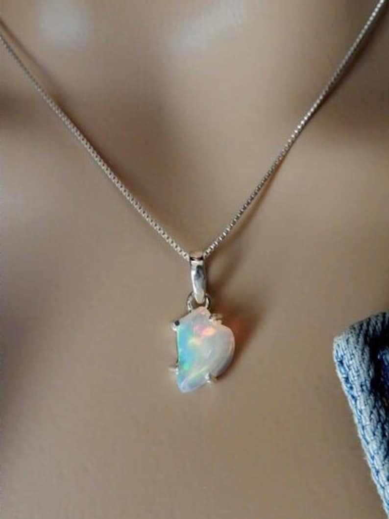 May include: A silver chain necklace with a pendant featuring a white opal gemstone with iridescent rainbow colors.