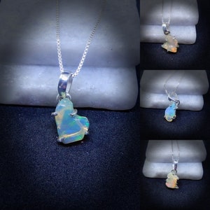 May include: A silver chain necklace with a pendant featuring a natural opal stone. The opal is a light blue-green color with flashes of rainbow.