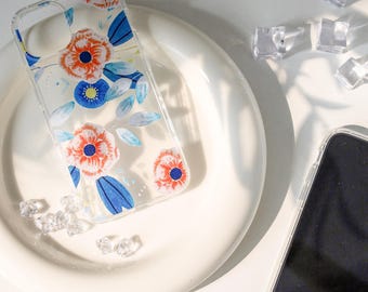 May include: A clear phone case with a floral design featuring blue and orange flowers on a white background.