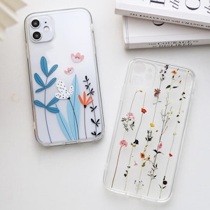 May include: Two clear phone cases with floral designs. The case on the left has a blue, white and orange floral design. The case on the right has a pressed flower design with various colours.