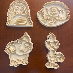 Pode incluir: Um conjunto de quatro cortadores de biscoitos de plástico bege com os contornos de uma personagem de cabelo comprido, uma personagem musculada com um colar, um porquinho e um galo. Cada cortador tem um rebordo elevado para a massa.