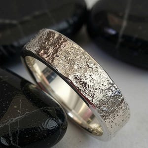 Handgemaakte ring van gesmolten zilver: unieke rustieke trouwring met een textuur van vloeibaar metaal.