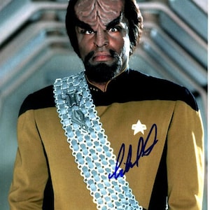 May include: A close-up of a man wearing a gold and black uniform with a silver sash and a star on the shoulder. He has a dark beard and a distinctive forehead ridge. The image is signed "LeVar Burton".
