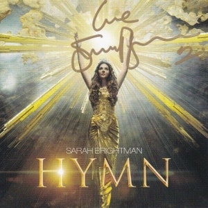 Puede incluir: Una mujer con un vestido dorado se encuentra de pie con los brazos en alto, bañada por una luz dorada. El texto "HYMN" está escrito en letras doradas grandes debajo de ella. El texto "SARAH BRIGHTMAN" está escrito en letras más pequeñas encima de la palabra "HYMN".