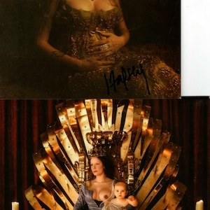 Puede incluir: Una mujer con un vestido dorado se sienta en un trono con un bebé en sus brazos. La mujer está amamantando al bebé. El trono está hecho de oro y tiene una corona en la parte superior. La mujer lleva una corona y un collar. El fondo es una cortina roja oscura.