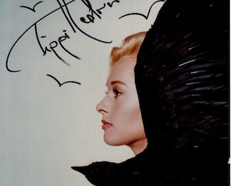 May include: A portrait of a woman in profile with blonde hair, a black bird wing, and an autograph that reads "Tippi Hedren". The signature is in black ink, with a heart and bird illustrations.