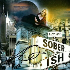 Puede incluir: Una mujer con un top rojo y pantalones negros posa frente a un telón de fondo de la ciudad de Nueva York. La imagen es un collage con un arco grande y letreros de calle que dicen "Lizphair" y "SOBER ISH".