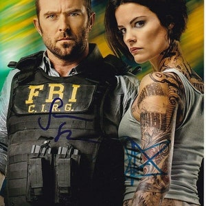 Puede incluir: Un póster promocional para la serie de televisión "Blindspot" con dos actores. El actor masculino lleva un chaleco negro con "FBI C.I.R.G." impreso en él. La actriz femenina lleva un top gris sin mangas y tiene tatuajes en los brazos. El póster tiene el título "Blindspot" impreso en la parte inferior.