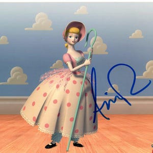 May include: A pink and white dress with polka dots and a blue and green shepherd's crook. The character is a doll with blonde hair and a pink hat. The background is a blue sky with white clouds. The image is signed "Annie".