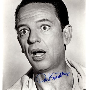 Pode incluir: Fotografia em preto e branco de Don Knotts, um ator americano, com uma expressão de surpresa. Ele está vestindo uma camisa branca e assinou seu nome em tinta azul abaixo da foto. O texto "The Reluctant Astronaut" está impresso abaixo da assinatura.