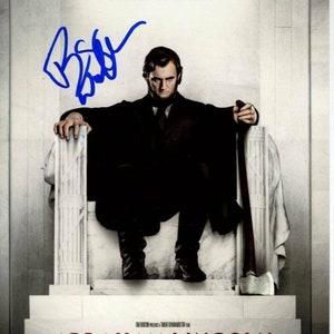 Könnte beinhalten: Ein Filmplakat für den Film "Abraham Lincoln: Vampire Hunter". Das Plakat zeigt einen Mann in einem schwarzen Anzug und Krawatte, der auf einem Thron sitzt und eine Axt in der Hand hält. Der Text auf dem Plakat lautet "Präsident bei Tag, Jäger bei Nacht." und "Abraham Lincoln: Vampire Hunter".