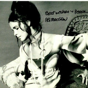 Może przedstawiać: Czarno-białe zdjęcie kobiety w jasnej sukience z gwiazdkami. Sukienka ma długie rękawy i dekolt w kształcie litery V. Kobieta siedzi na wiklinowym krześle i ma na szyi perłowy naszyjnik. Zdjęcie jest podpisane "Ali MacGraw" ze słowami "Best wishes and Peace".