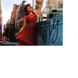 Puede incluir: Una mujer con un vestido rojo sostiene una estrella dorada frente a un fondo de ciudad. La portada del álbum presenta el texto "I Dream of Christmas" y "Norah Jones".