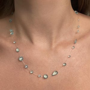 May include: A delicate necklace featuring a thin, transparent cord adorned with scattered, light green, translucent beads in various shapes, including small circles and teardrops, spaced unevenly along the length of the jewelry piece.