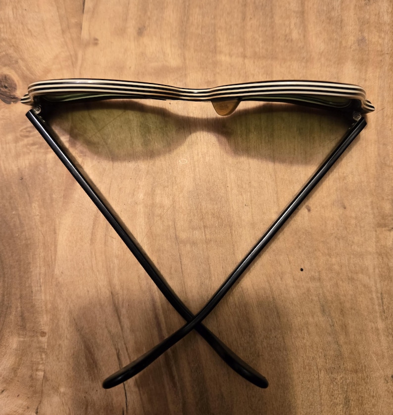 May include: Black and white striped sunglasses with black frames. The sunglasses are folded in half and the frames are crossed.