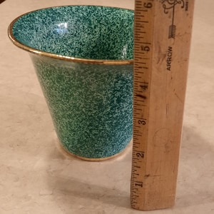 May include: A green ceramic planter with a gold rim. The planter is speckled with white and has a slightly flared top. It is 5 inches tall.