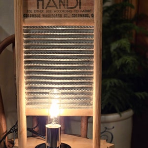 May include: A wooden washboard lamp with a light bulb turned on. The washboard has the text "DUBL HANDI USE EITHER SIDE ACCORDING TO FABRIC COLUMBUS WASHBOARD CC., COLUMBUS, O" printed on it.