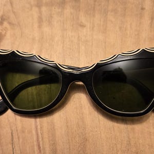 May include: Black cat-eye sunglasses with a white and black wavy design on the frame.
