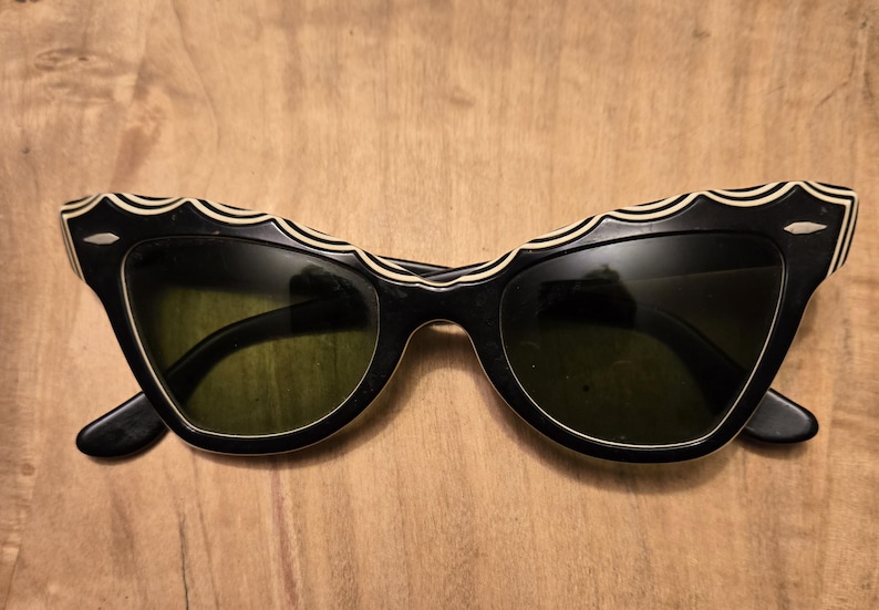 May include: Black cat-eye sunglasses with a white and black wavy design on the frame.