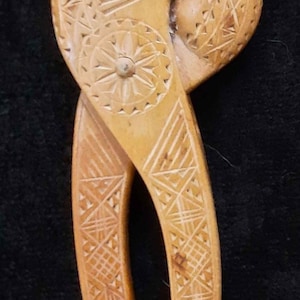 May include: A wooden nutcracker with intricate carvings. The nutcracker is shaped like a bird's head with a beak that opens to crack nuts. The handles are carved with geometric patterns.