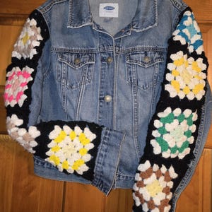 May include: A blue denim jacket with crocheted sleeves. The sleeves are made of colorful squares in shades of pink, yellow, green, brown, and white.