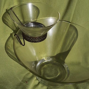 May include: A clear glass serving bowl set with a smaller bowl suspended above a larger bowl. The smaller bowl is held by a decorative metal stand. The set is designed for serving dips and snacks.