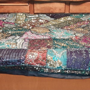 May include: A colorful patchwork throw blanket with sequins and embroidery. The blanket is made of various fabrics in shades of green, blue, purple, red, and gold.