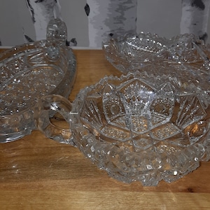 May include: Three clear glass bowls with intricate cut glass designs. The bowls have two handles and are perfect for serving snacks or desserts.