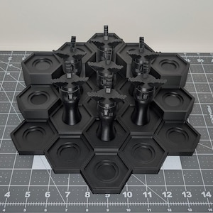 May include: Black hexagonal display stand with multiple compartments and six black decorative objects. The stand is made of a matte black material and is arranged in a honeycomb pattern. The objects have a unique, stylized design.