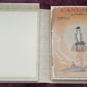 May include: An open, linen-covered box with a book titled "Candide par Voltaire." The book cover features an illustration of a figure in a green coat and hat, with the title in red and the author's name in black.