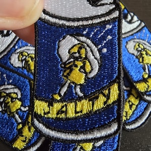 Op de afbeelding: Een set van vier geborduurde strijklabels met een blauwe en gele blik met het woord "SALTY" erop. De blik heeft een wit deksel en een gele figuur erin.