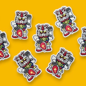 Op de afbeelding: Tien geborduurde patches met een cartoonrobot in een wit, rood en blauw kleurenschema. De robot houdt een zwaard en een schild vast. De patches bevinden zich op een gele achtergrond.