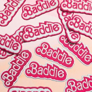 Pode incluir: Um conjunto de patches termocolantes rosa e branco com a palavra "Baddie" escrita em letra cursiva.