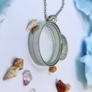 May include: A silver locket necklace with a clear glass centre, adorned with tiny seashells and colourful gemstones. The necklace hangs from a delicate chain, creating a beachy, bohemian aesthetic.