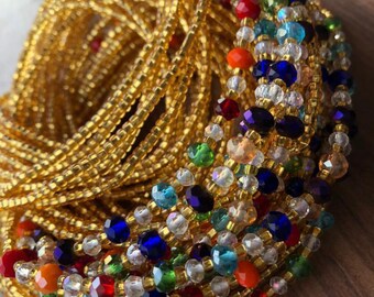 Puede incluir: Una cadena de cintura de cuentas doradas con cuentas de vidrio de colores. Las cuentas son en tonos de rojo, naranja, amarillo, verde, azul y morado.