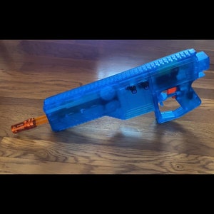 May include: A blue transparent toy gun with an orange barrel. The gun has a textured grip and a black trigger.