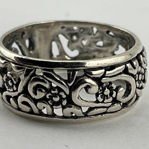 May include: A silver ring featuring an intricate floral design. The ring is crafted from a delicate, openwork design with a floral pattern.