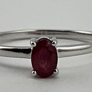 Op de afbeelding: Een zilveren ring met een rode ovale edelsteen.