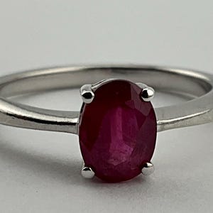 May include: A silver ring featuring a deep red oval ruby gemstone.