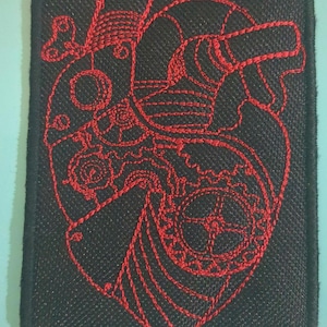 May include: Red embroidered patch of a stylized human heart with gears and other mechanical elements. The patch is on a black background.