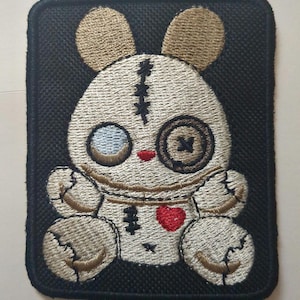 Könnte beinhalten: Ein gestickter Aufnäher mit einem zusammengenähten Hasen mit einem roten Herzen, einem Knopfauge und einem zusammengenähten Mund. Der Hase sitzt auf einem schwarzen Hintergrund.