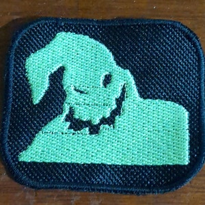 May include: A black and green embroidered patch featuring a silhouette of a ghost with a mischievous grin.