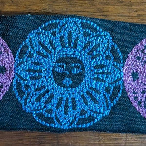 May include: A black fabric patch with a triple moon design embroidered in purple and blue thread. The moon is a crescent shape with a face in the center. The sun is a circle with a face in the center.
