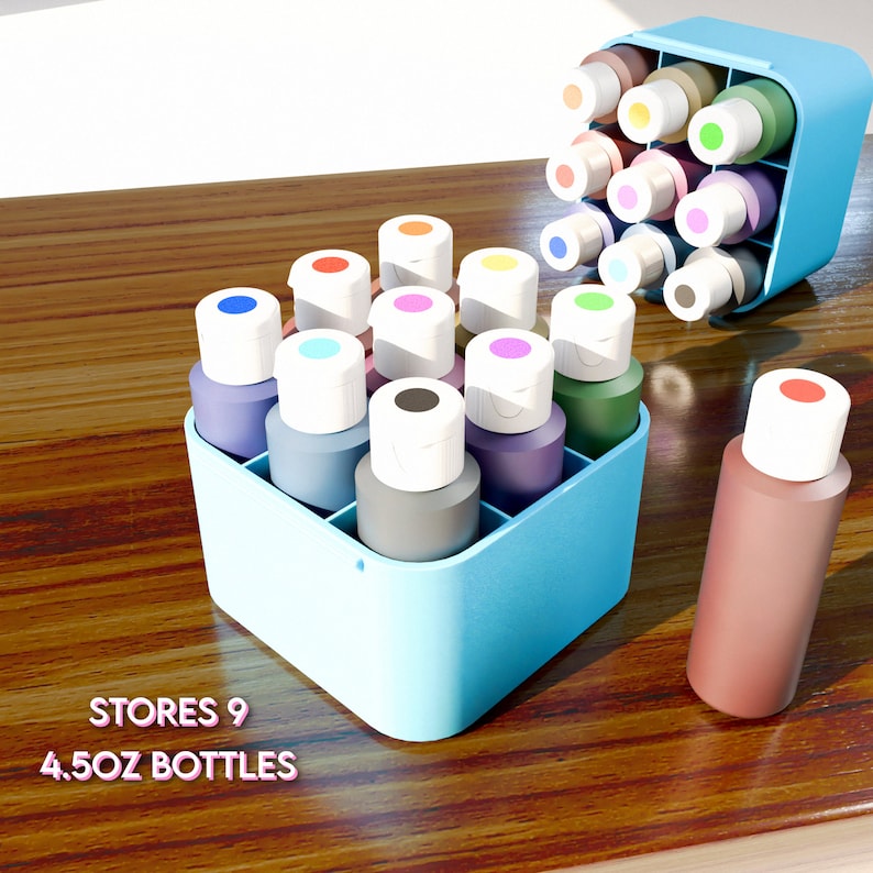 May include: A blue plastic organizer with nine 4.5 oz bottles of paint. The bottles are arranged in a grid pattern and have white lids. The organizer is sitting on a wooden surface. The text "STORES 9 4.5OZ BOTTLES" is printed on the surface.