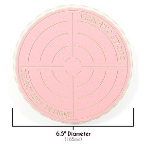 Op de afbeelding: Een roze en groene koekjescarrousel met een diameter van 16,5 cm. De carrousel is ontworpen om koekjes te bewaren en heeft een cirkelvormig ontwerp met concentrische cirkels. De tekst "Cookie Carousel" en "Delectable Designs" staat op de carrousel gedrukt.