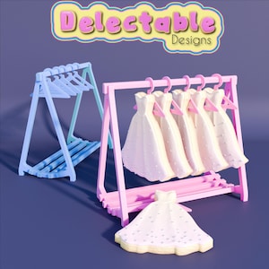 Może przedstawiać: Różowy drewniany stojak na ubrania z pięcioma białymi sukienkami wiszącymi na wieszakach. Sukienki mają koralikowy wzór. Mniejsza biała sukienka z koralikowym wzorem leży na podłodze przed stojakiem. Stojak stoi na fioletowym tle.  Delectable Designs jest napisane żółtymi literami na różowo-żółtym tle.