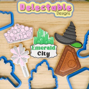May include: A set of cookie cutters featuring various designs from the Wizard of Oz, including a crown, a witch's hat, the Emerald City, and a magic wand. The cutters are made of blue plastic and are arranged on a wooden surface.