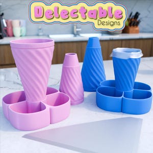 Puede incluir: Dos juegos de soportes para conos de helado de silicona rosa y azul. Cada juego incluye un soporte para conos, un soporte para conos más pequeño y una base de cuatro secciones. La base tiene cuatro compartimentos para guardar cucharas de helado. El texto "Delectable Designs" es visible en la parte superior de la imagen.