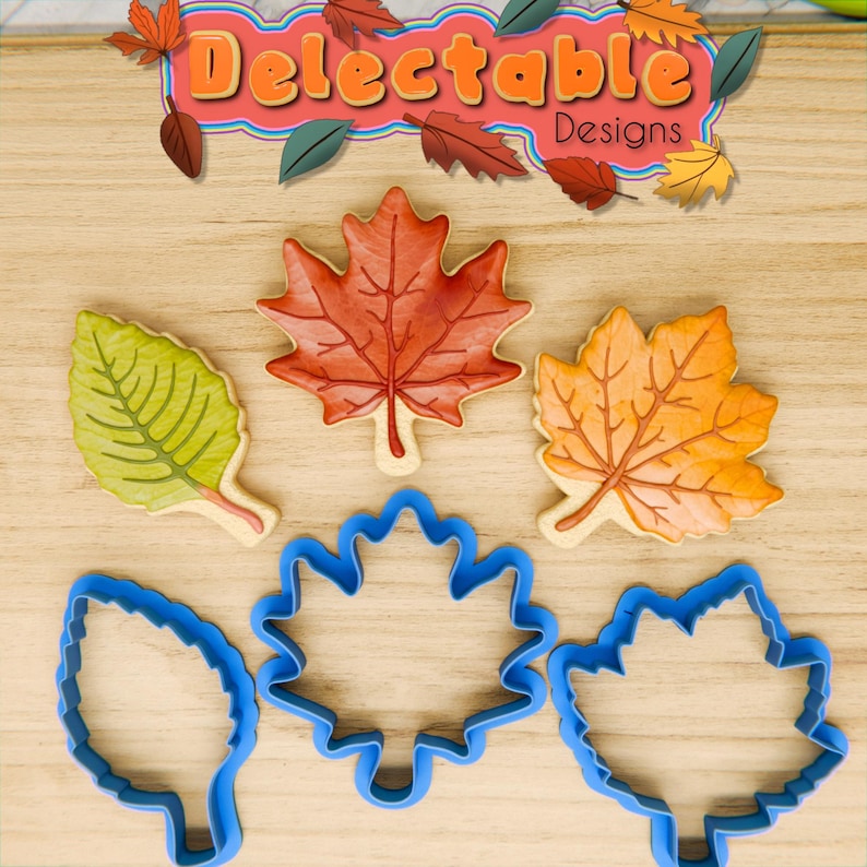May include: Four cookie cutters in the shape of leaves. Two are maple leaves, one is a simple leaf, and one is a more detailed leaf. The cutters are blue and are on a wooden surface.