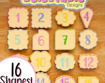 May include: A set of 16 cookie cutters in various shapes, numbered 1 through 16. The cutters are made of a light yellow material with a white outline and are arranged on a wooden surface. The text "Delectable Designs" is at the top of the image.